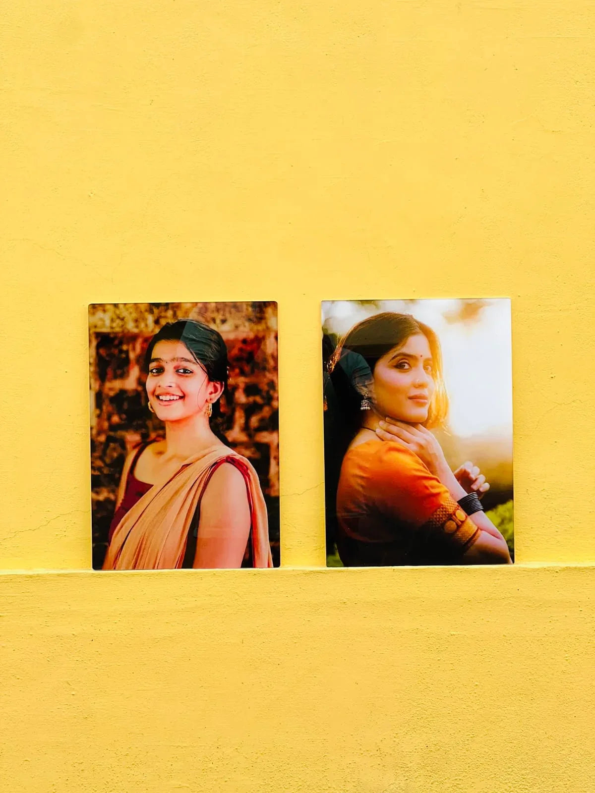 Two portrait photo frames with women in traditional attire on a yellow wall background