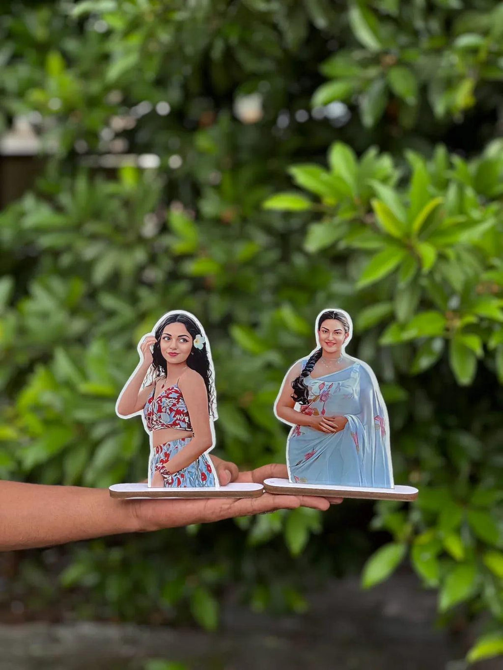 Custom photo frame cutouts of women in colorful outfits, displayed outdoors in hand
